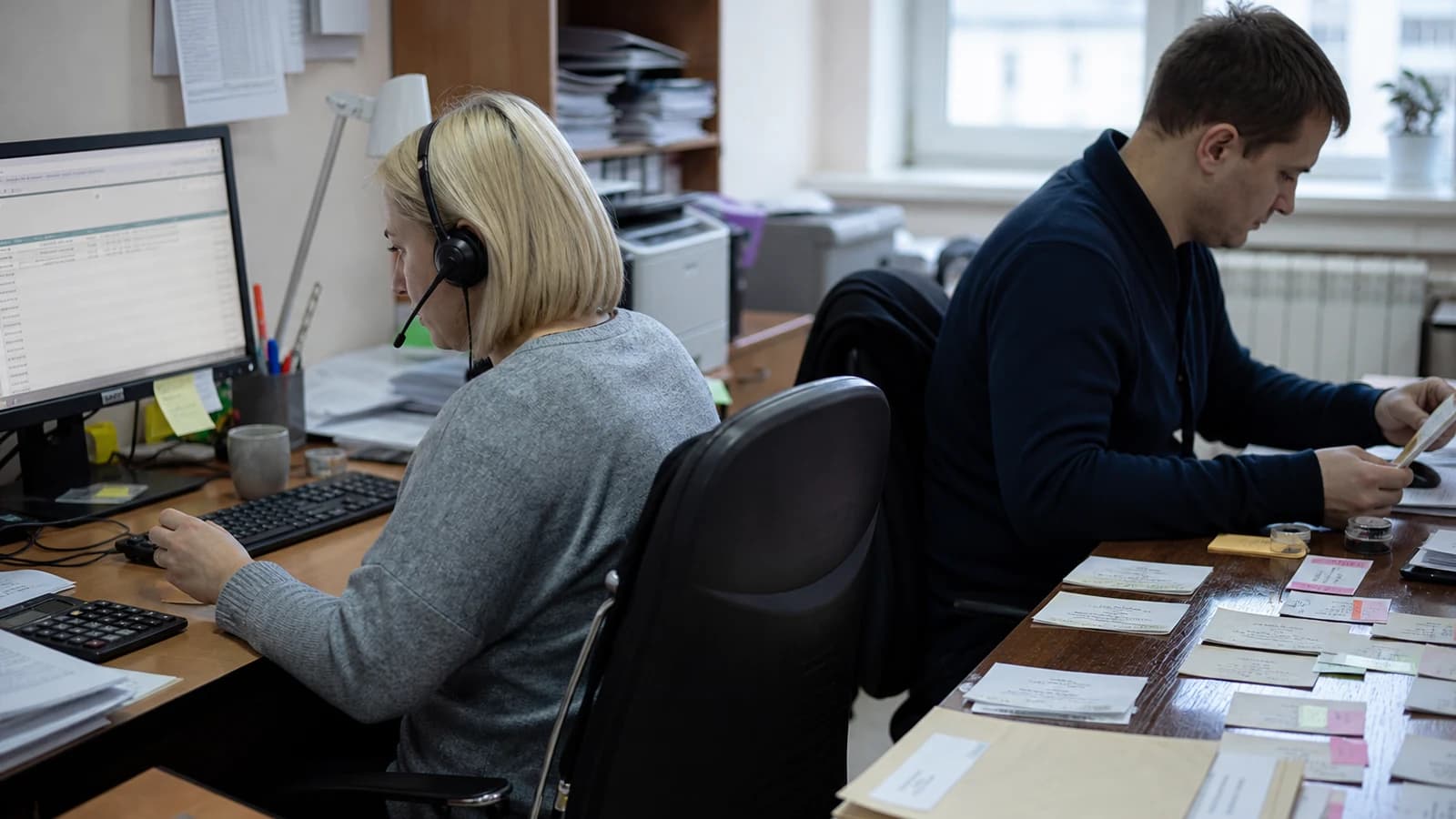 Два сотрудника обрабатывают долговые дела за соседними рабочими столами.