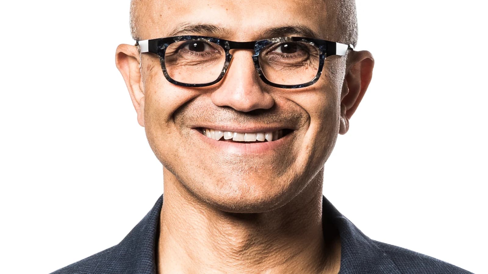 Портрет генерального директора Microsoft Сатьи Наделлы в очках на светлом фоне.