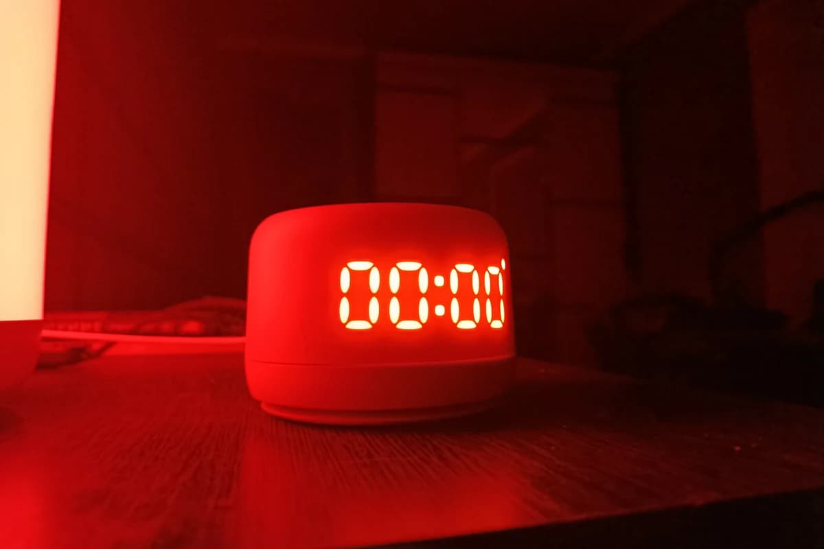 Красная умная колонка с цифровым дисплеем «00:00» на столе в тёмной комнате