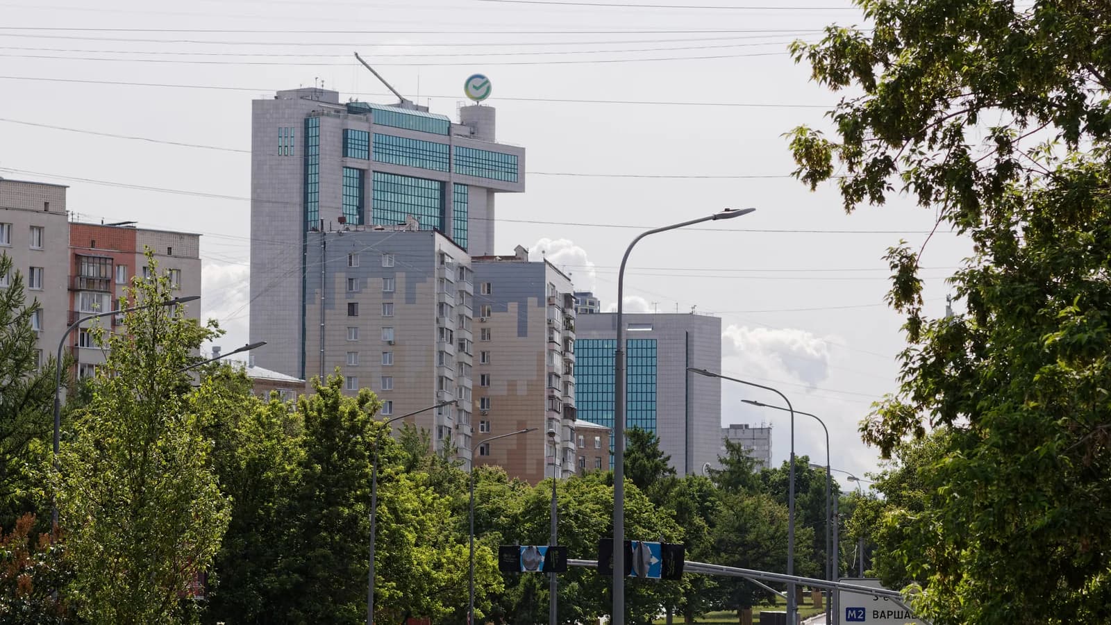 Высотное офисное здание с логотипом Сбера среди городской застройки и зелени