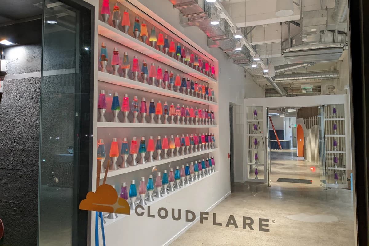 Вывеска Cloudflare на стекле у стены с разноцветными лавовыми лампами