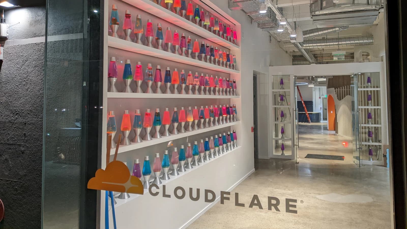 Вывеска Cloudflare на стекле у стены с разноцветными лавовыми лампами