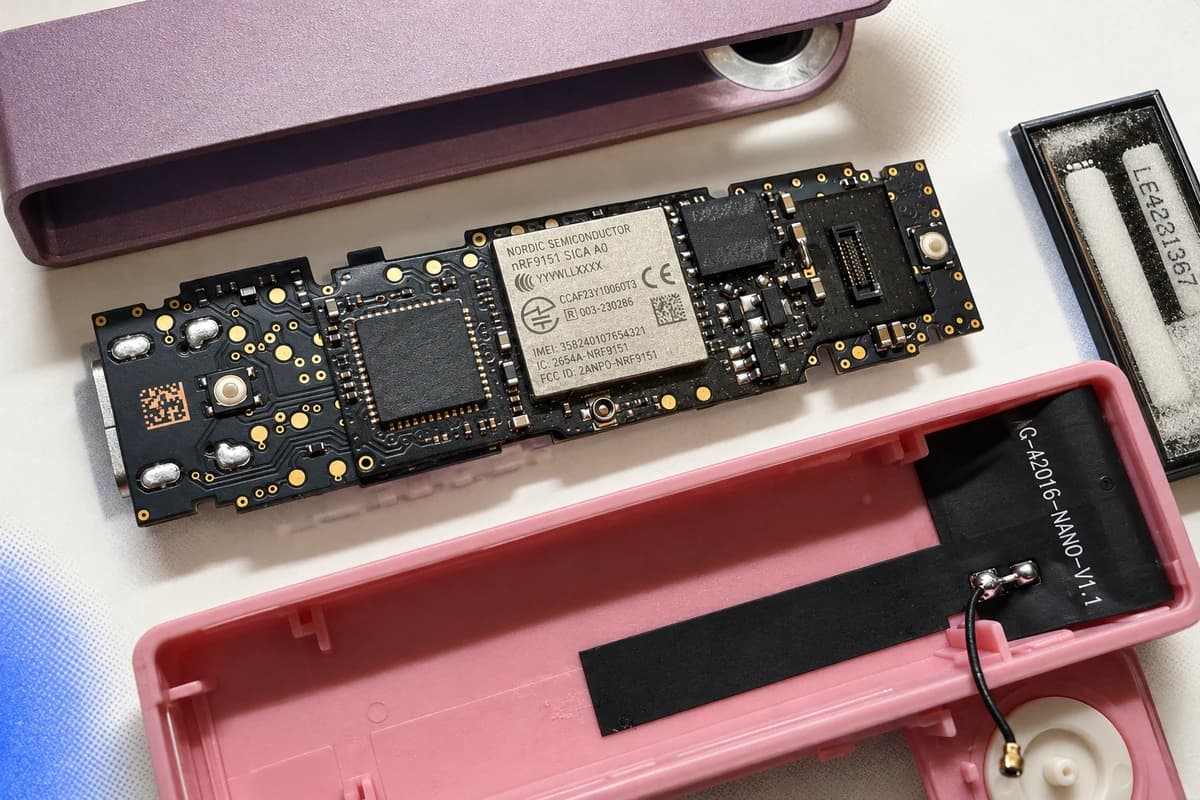Разобранный кошелёк Ledger с чёрной печатной платой, модулем Nordic nRF9151 и проводным элементом в розово-фиолетовом корпусе.