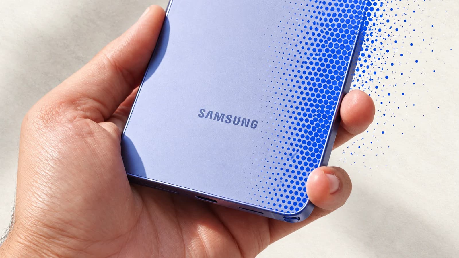 Светло-фиолетовый смартфон Samsung в руке, правая часть корпуса постепенно растворяется в синих растровых точках.
