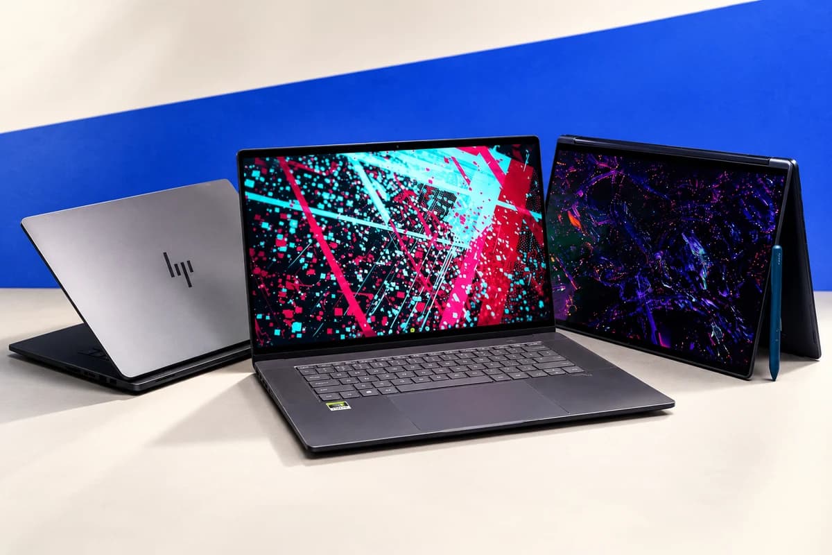 Три ноутбука на светлом столе: закрытый серебристый HP, открытый тёмный ноутбук с наклейкой Nvidia и трансформер со стилусом.
