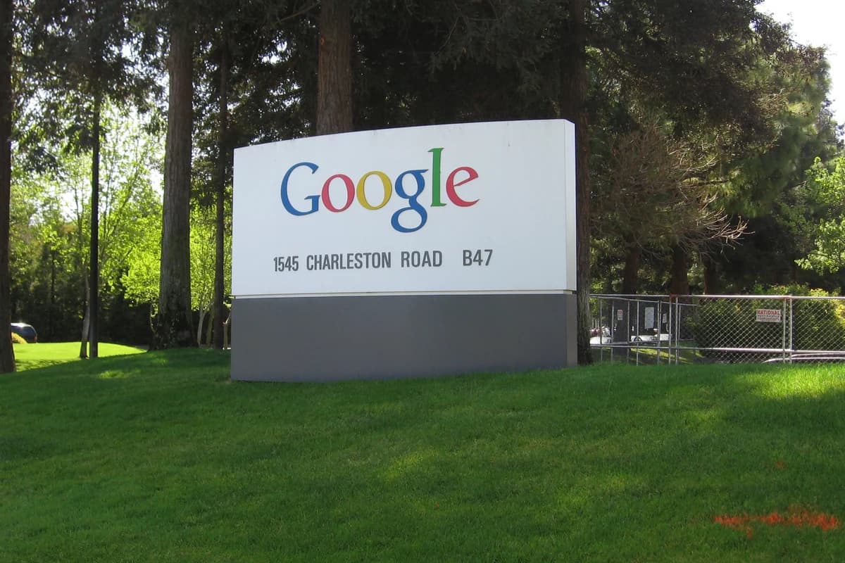 Вывеска с цветным логотипом Google на фоне деревьев и газона