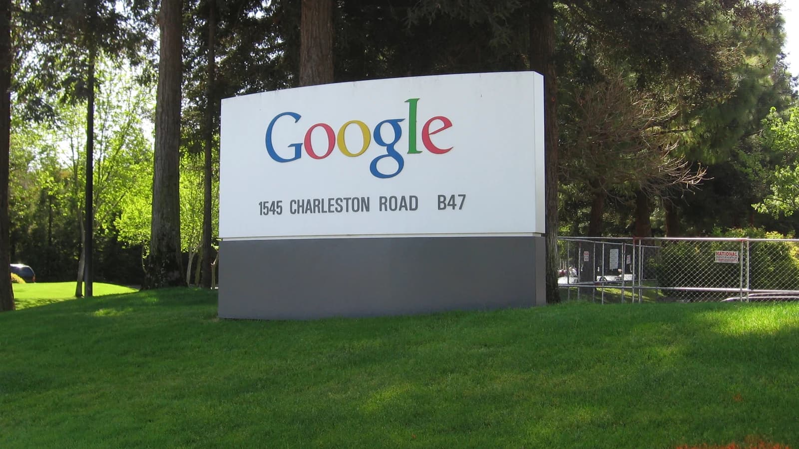 Вывеска с цветным логотипом Google на фоне деревьев и газона