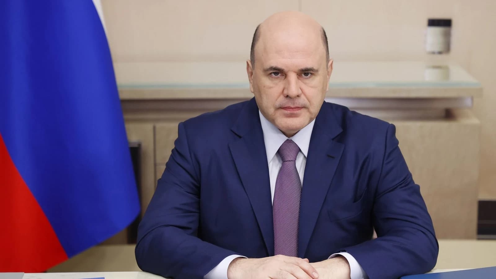 Михаил Мишустин сидит за столом на фоне российского флага