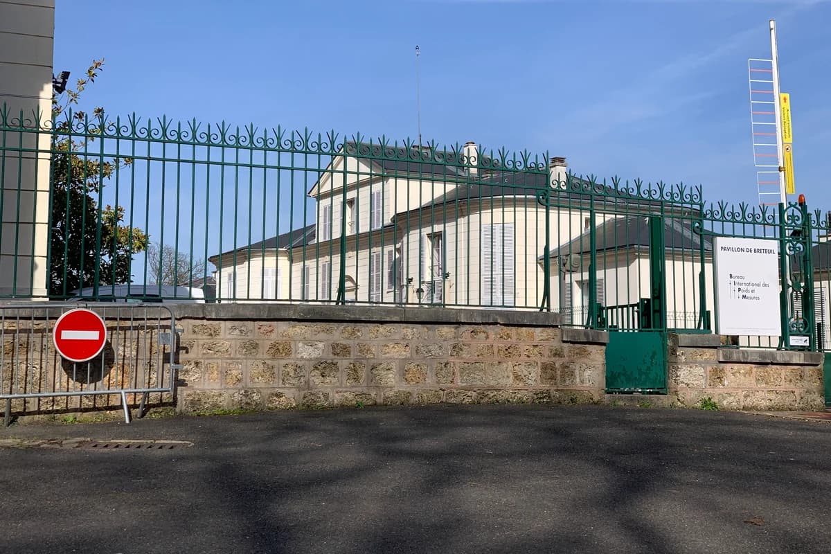 Светлое здание за зелёной оградой с табличкой «Pavillon de Breteuil»