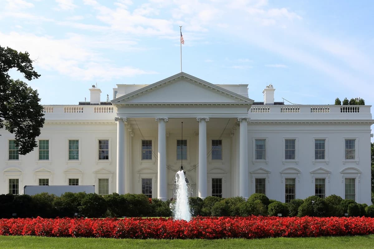 Белый дом с флагом США, фонтаном и красными цветами перед фасадом