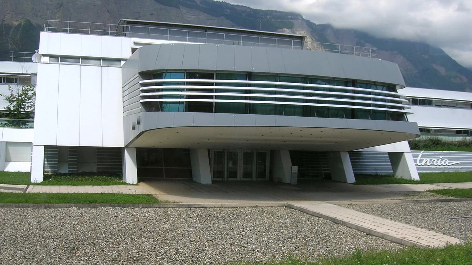 Здание исследовательского центра с вывеской Inria на фоне гор