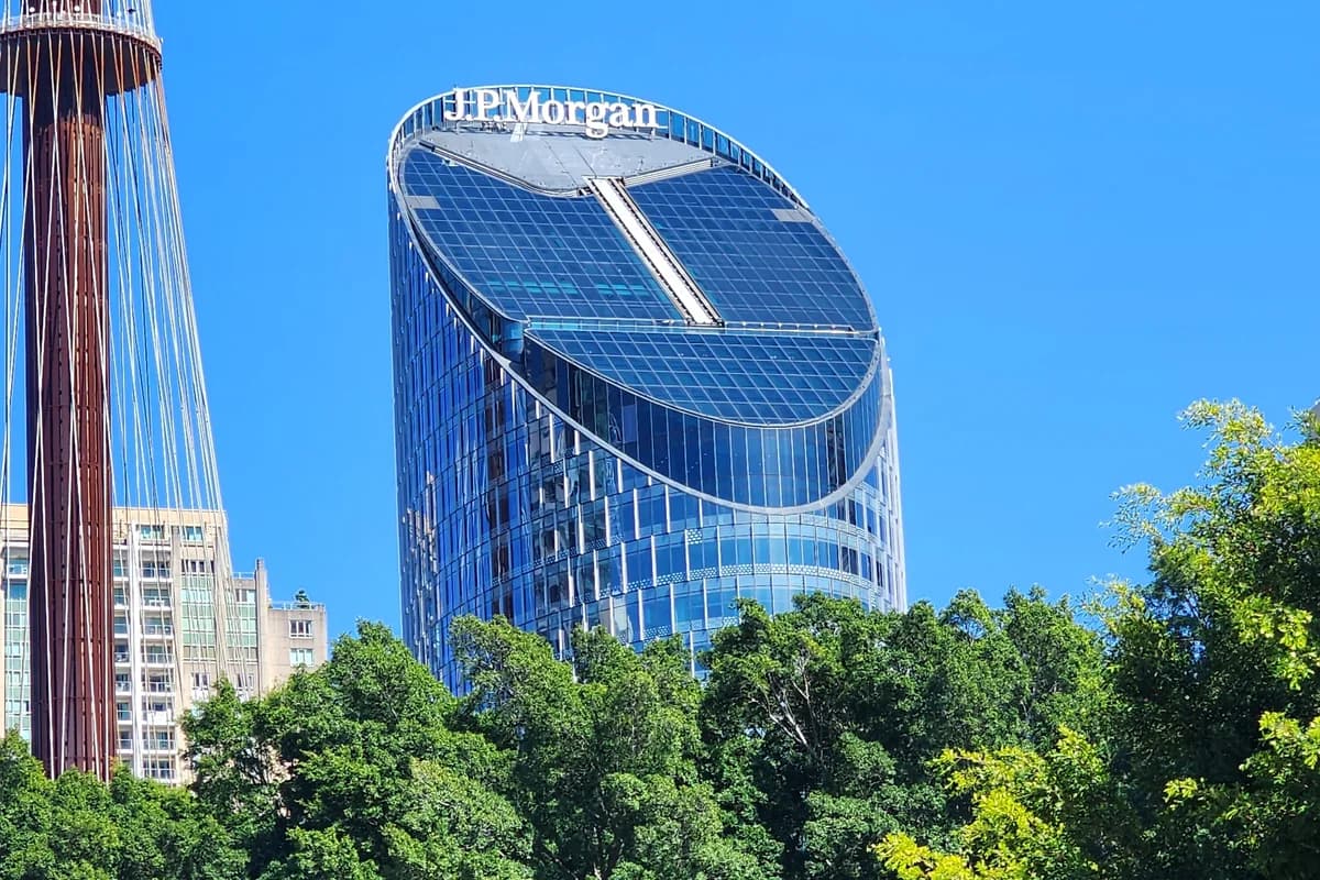 Стеклянное офисное здание с вывеской J.P. Morgan за зелёными деревьями